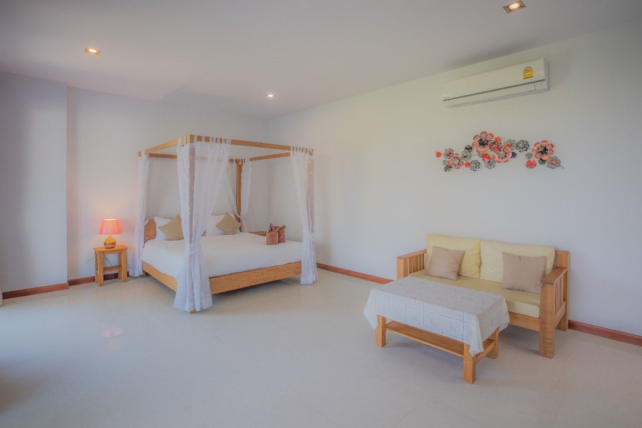 Bright bedroom with four-poster bed at Proud IV Pool Villa, Hua Hin. Features a sofa and decorative wall art.