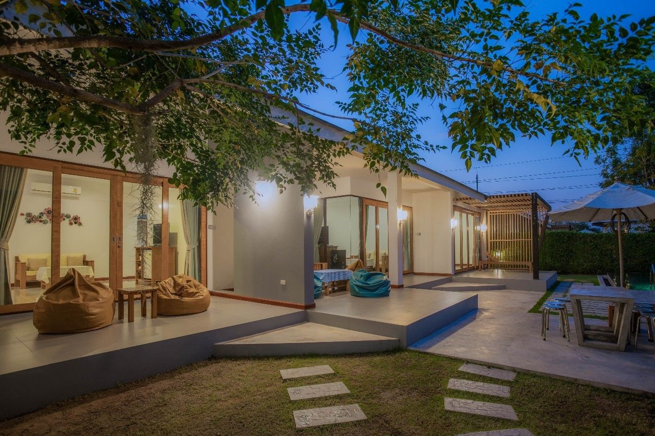Exterior view of Proud IV Pool Villa in Hua Hin at dusk, showing patio, beanbag chairs, and garden.