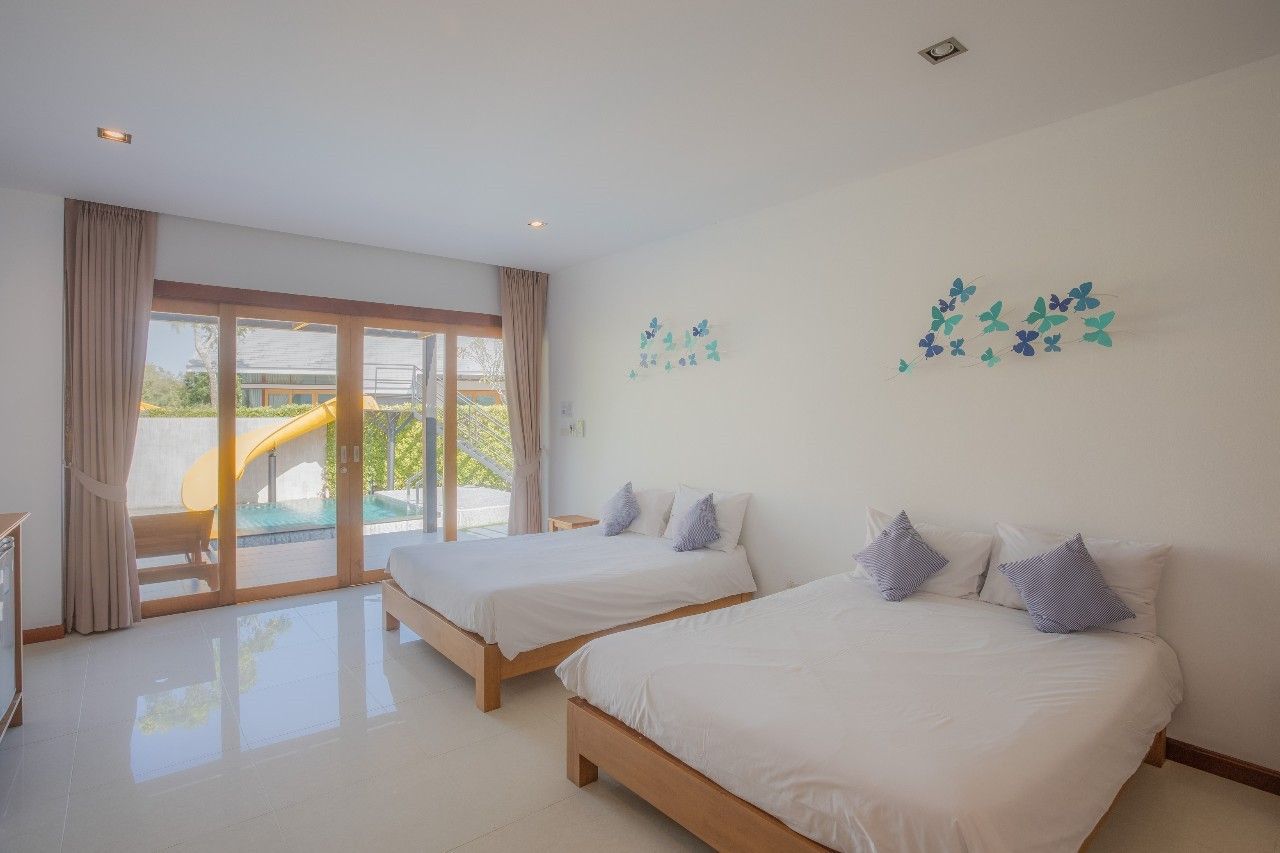 Bright bedroom with two beds at Proud IV Pool Villa, Hua Hin. Pool slide visible through sliding glass doors.