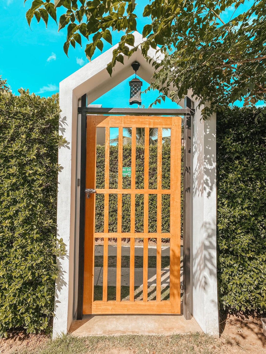 Entrance to Proud IV Pool Villa in Hua Hin, Thailand, featuring a wooden gate and lush green hedges.