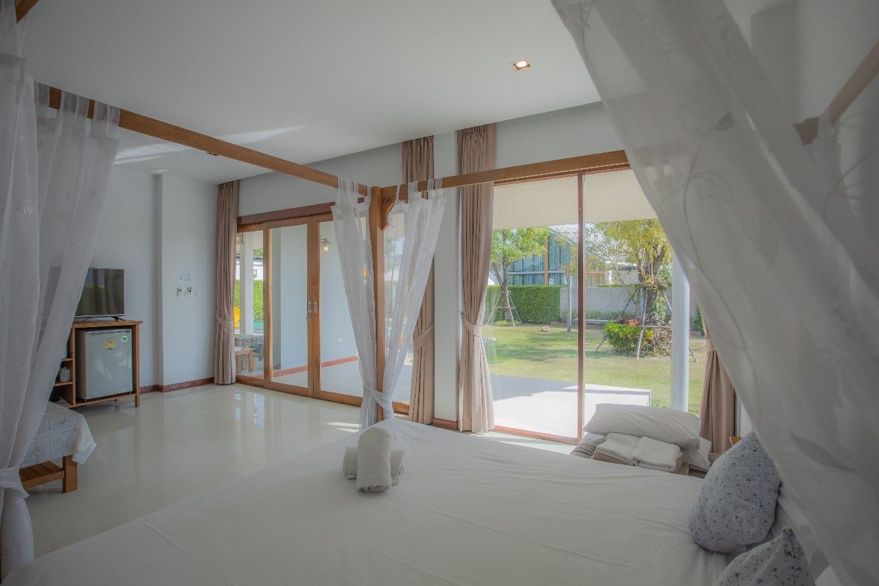 Bright bedroom with garden view at Proud V Pool Villa, Hua Hin. White linens and curtains create an airy feel.
