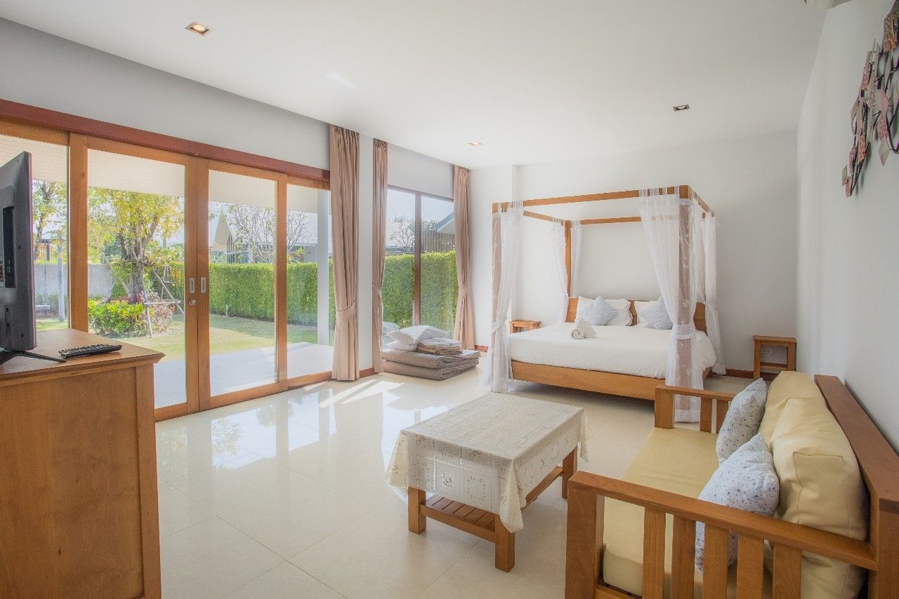 Bright bedroom suite with four-poster bed at Proud V Pool Villa, Hua Hin. Sliding doors open to the garden.