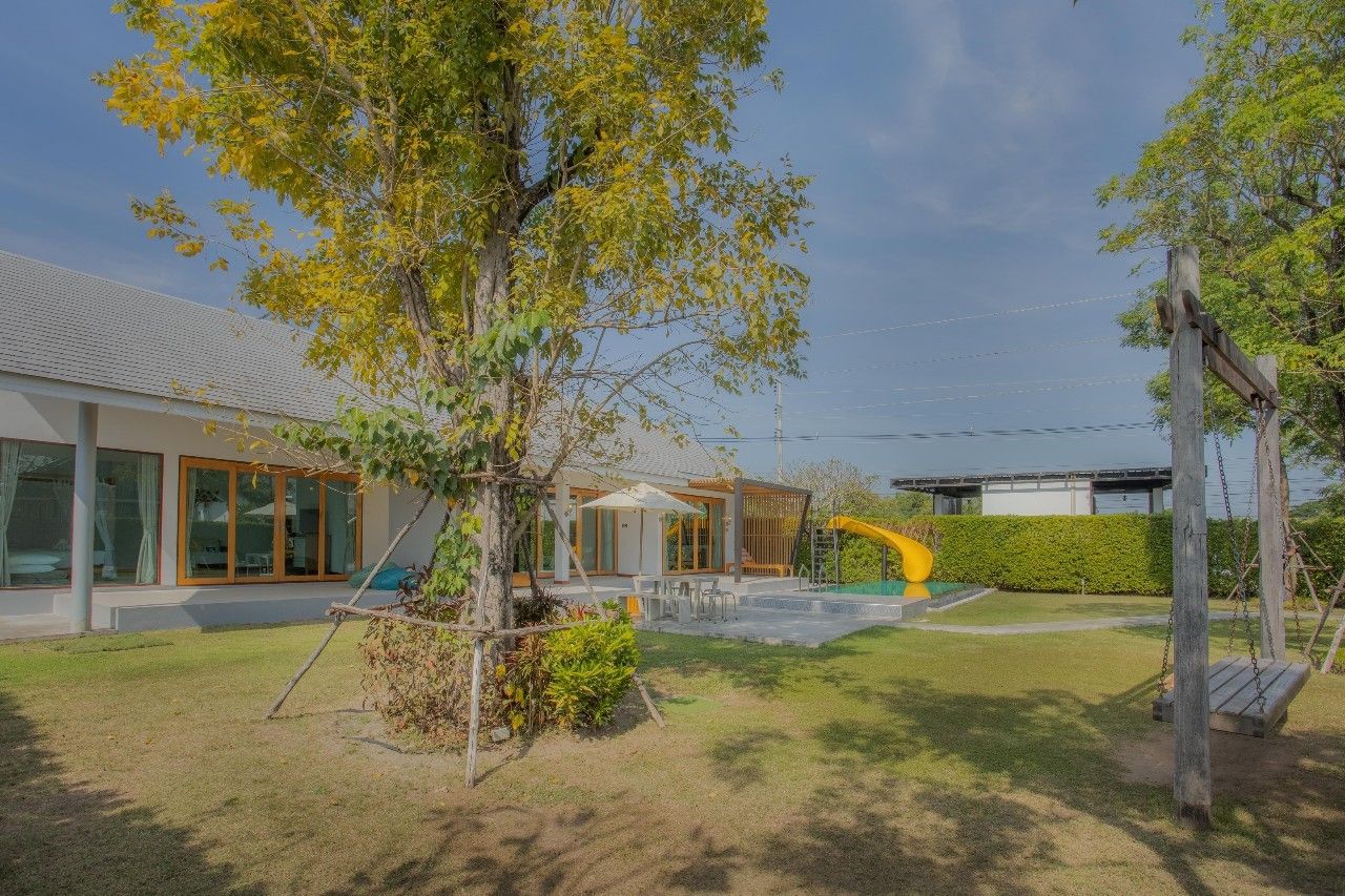 Lush lawn and playground at Proud V Pool Villa, Hua Hin. Features a slide, swing, and outdoor dining area.