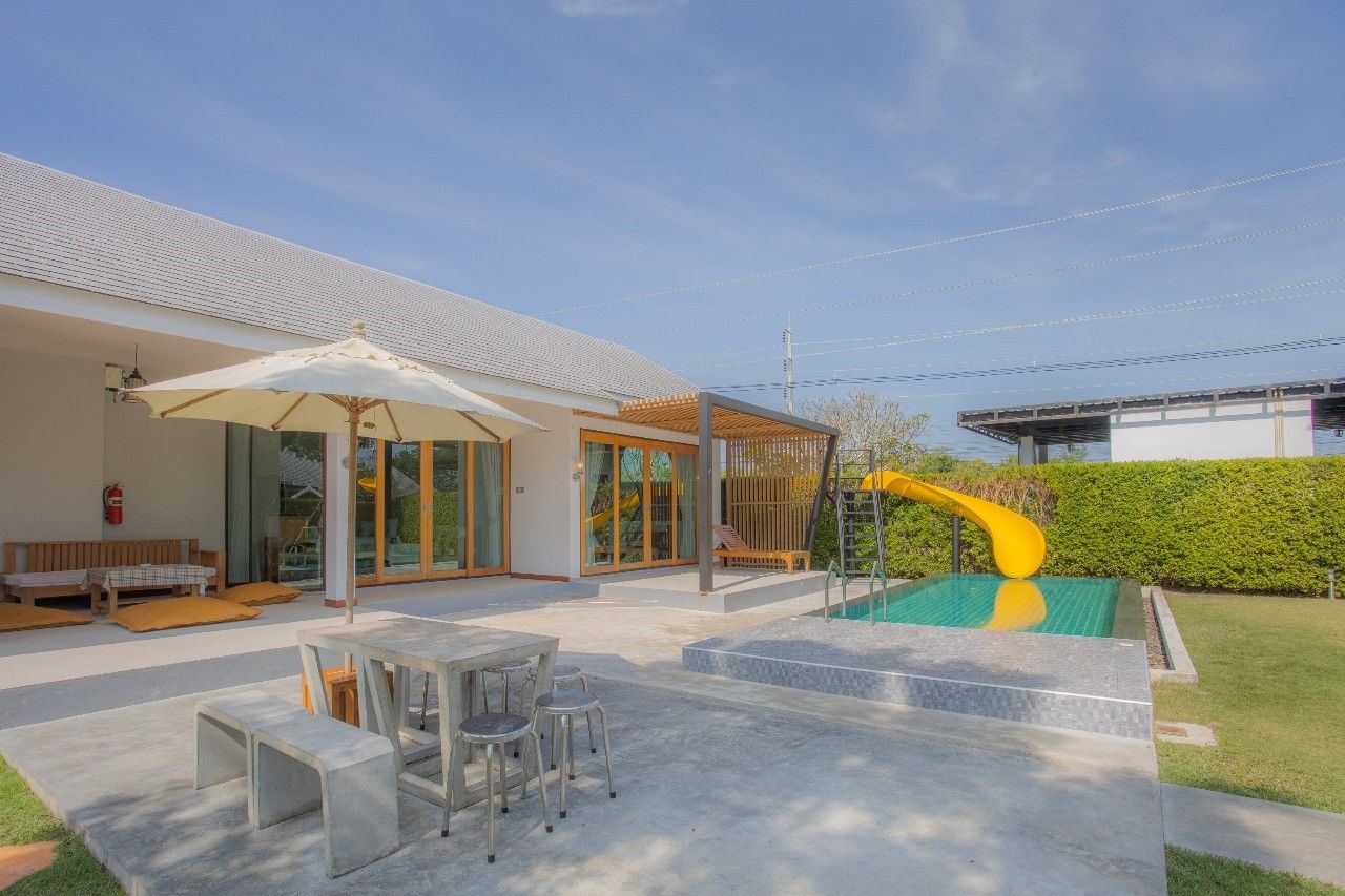 Outdoor pool with yellow slide at Proud V Pool Villa, Hua Hin. Seating area and manicured lawn visible.