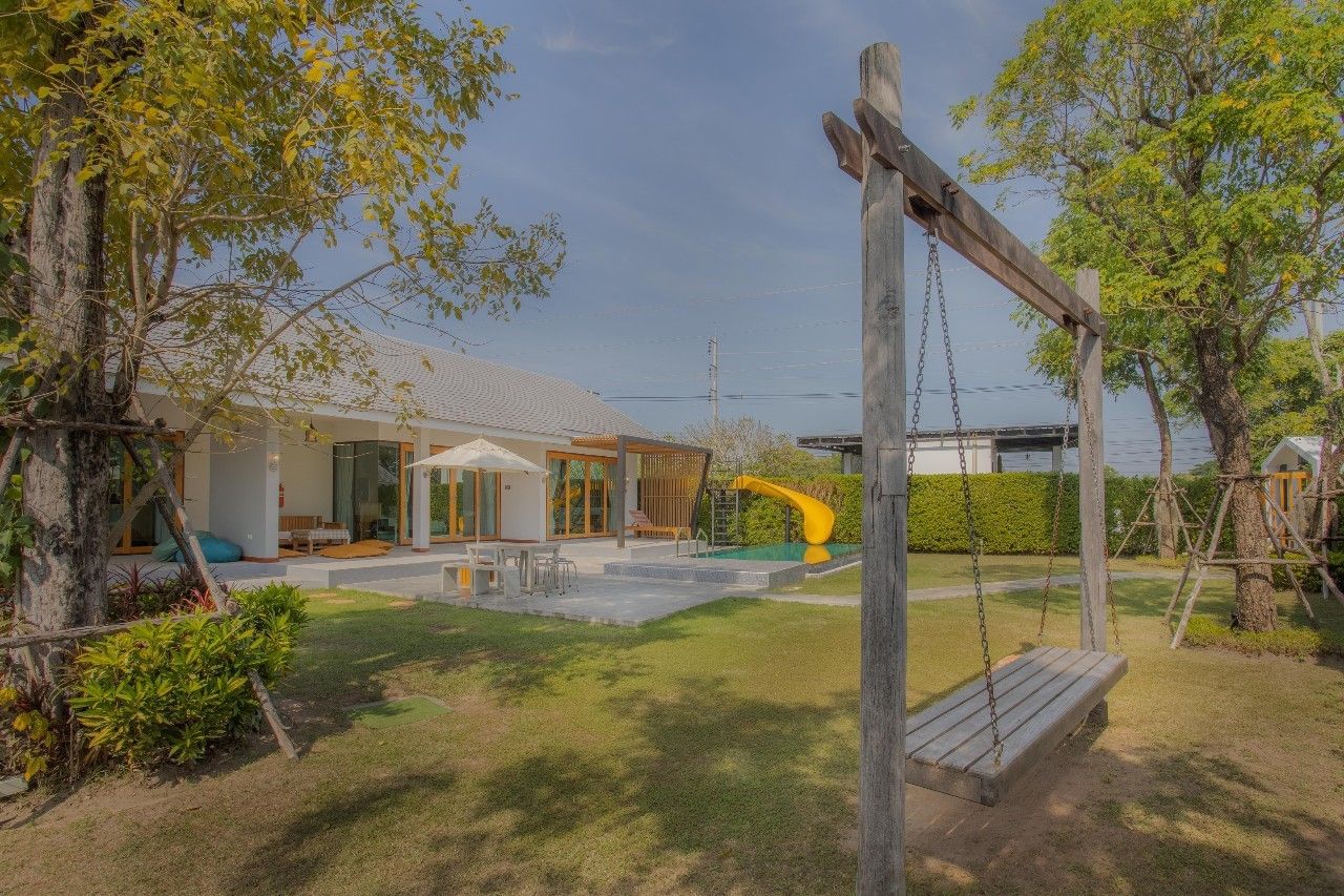 Lawn with swing set and slide at Proud V Pool Villa, Hua Hin. Outdoor dining and villa in background.