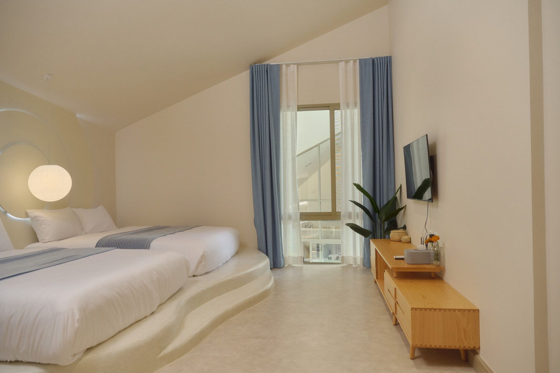 Roove V Pool Villa bedroom near Khaoyai National Park features two twin beds on a raised platform. Blue curtains and TV.