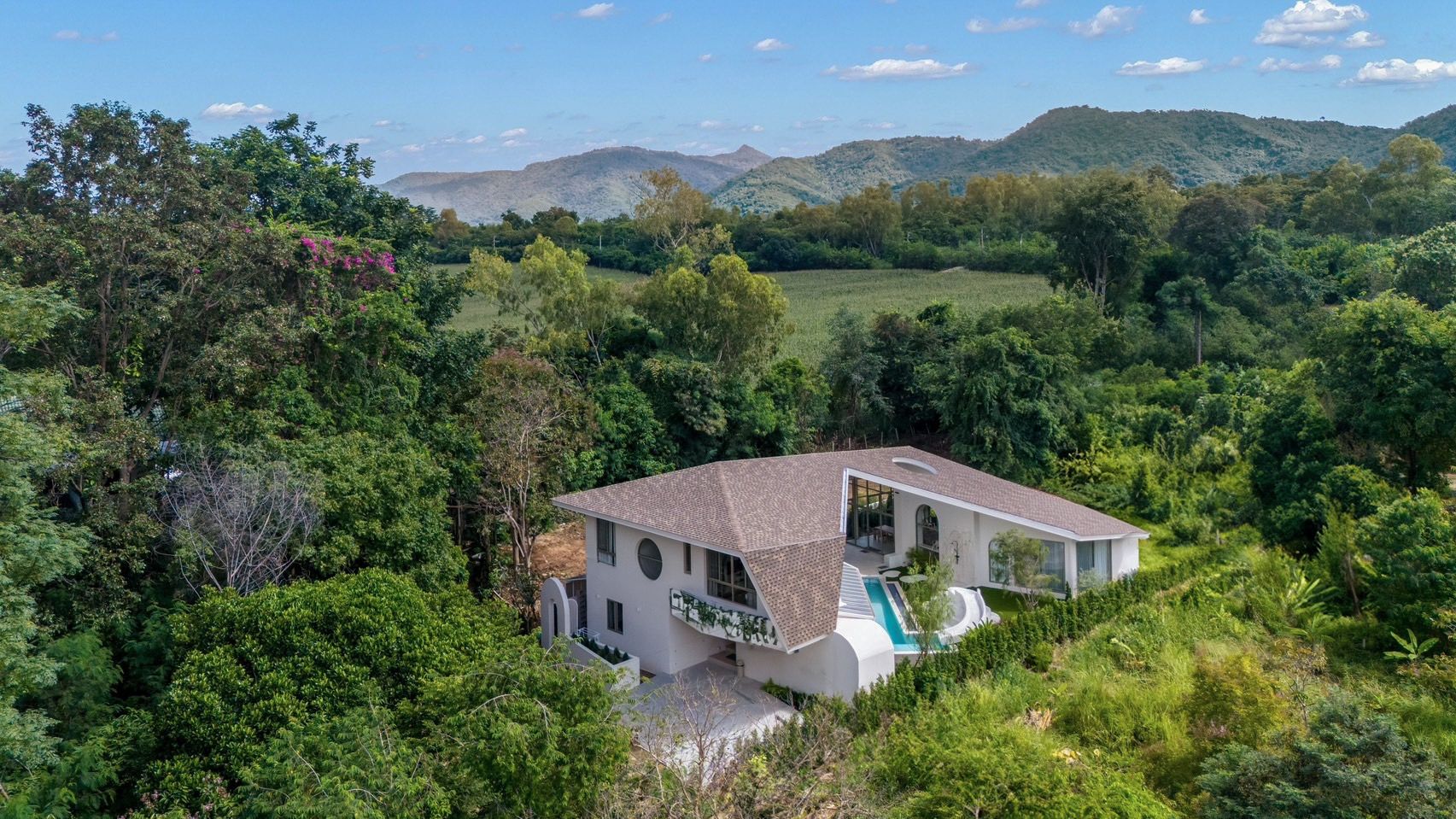 Aerial view of Roove V Pool Villa near Khaoyai National Park. Modern white villa nestled in lush green landscape with mountai