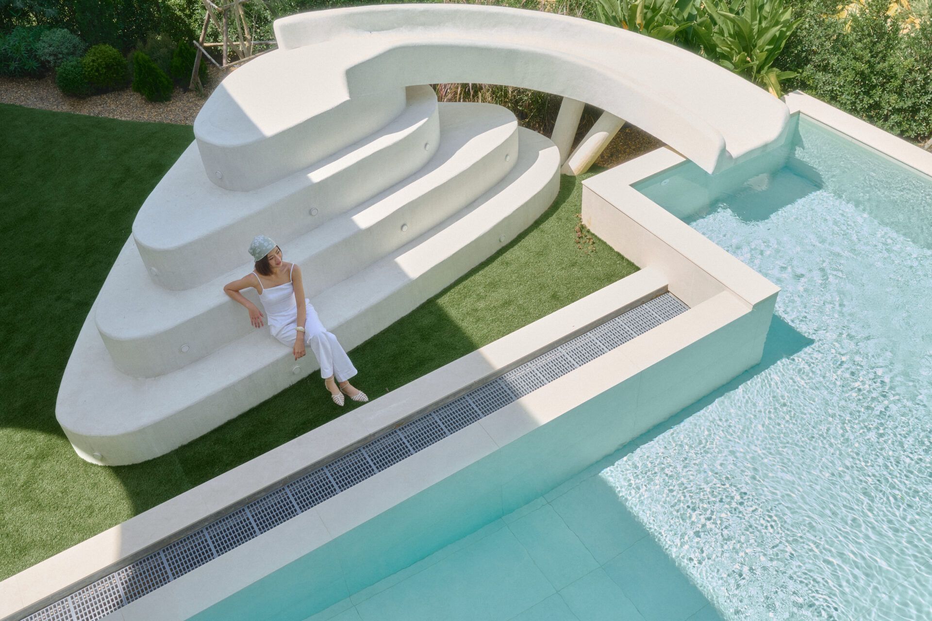 Woman sits on the water slide steps at Roove V Pool Villa near Khaoyai National Park. View of the pool and slide.