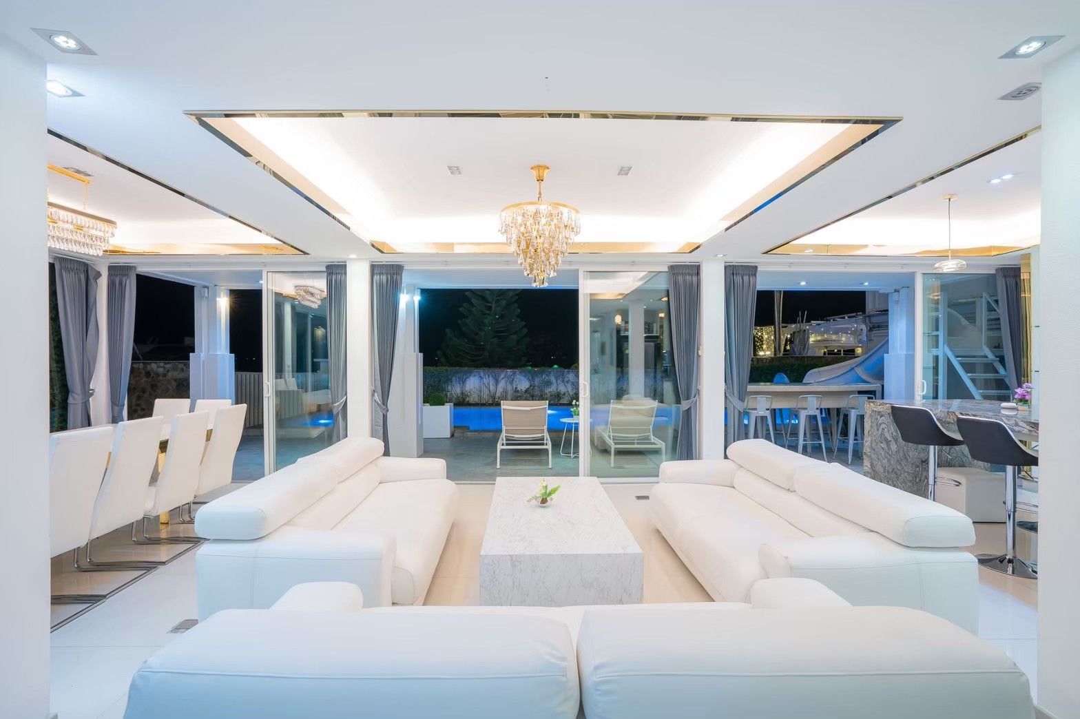 Royal Beach X Pool Villa living room at night. White leather sofas and view of the pool area in Pattaya.