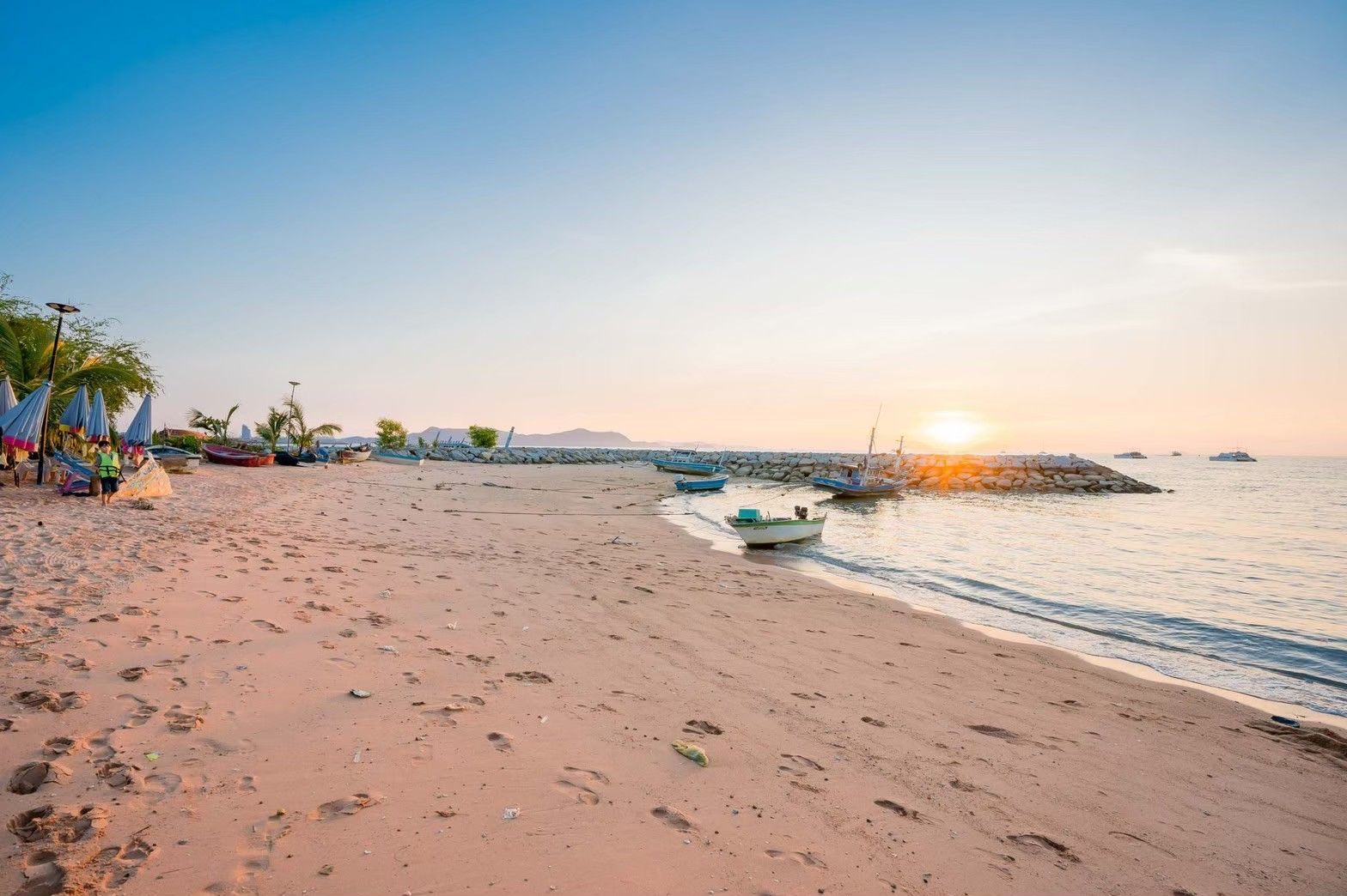 Sunset view of the beach near Royal Beach X Pool Villa, ติดทะเลนาจอมเทียน พัทยาใต้. Fishing boats on the sand.