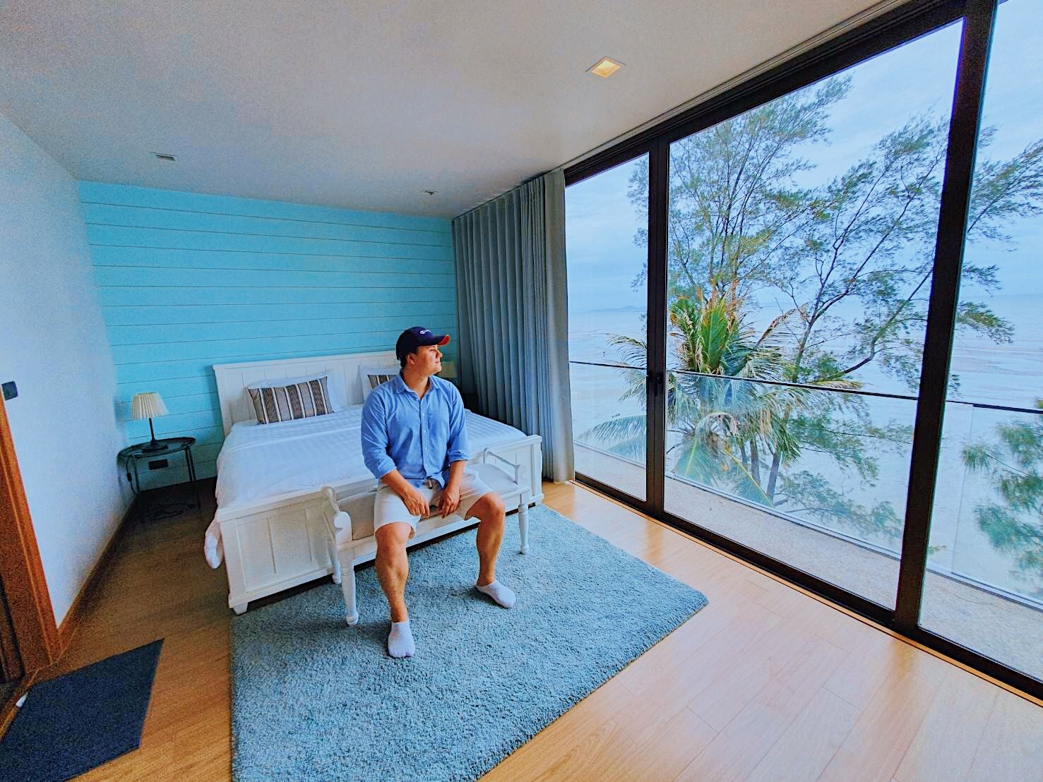 Bedroom with ocean view at Sand Beachfront Pool Villa III, ติดทะเลพัทยาเหนือ บางละมุง. Man sitting on bed looking out window.