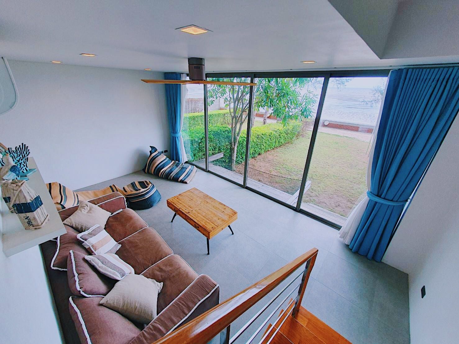 Living room with ocean view at Sand Beachfront Pool Villa III, North Pattaya. Modern sofa, beanbags, and wood table.
