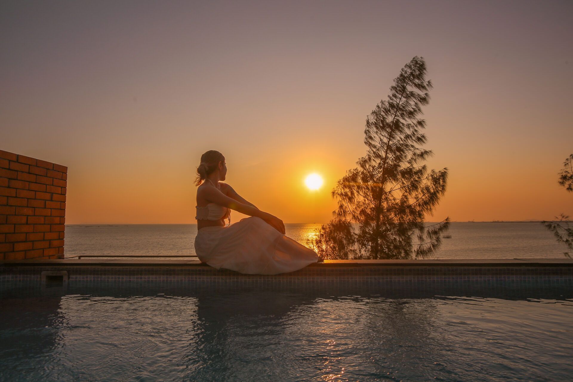 Woman sits at Sand Beachfront Villa IV pool edge, watching the sunset in Pattaya, Thailand.