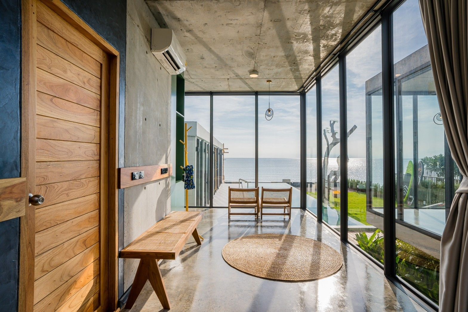 Hallway with ocean view at Sea Fan IV Beachfront Pool Villa near Huahin airport. Bench, rug, and floor-to-ceiling windows.