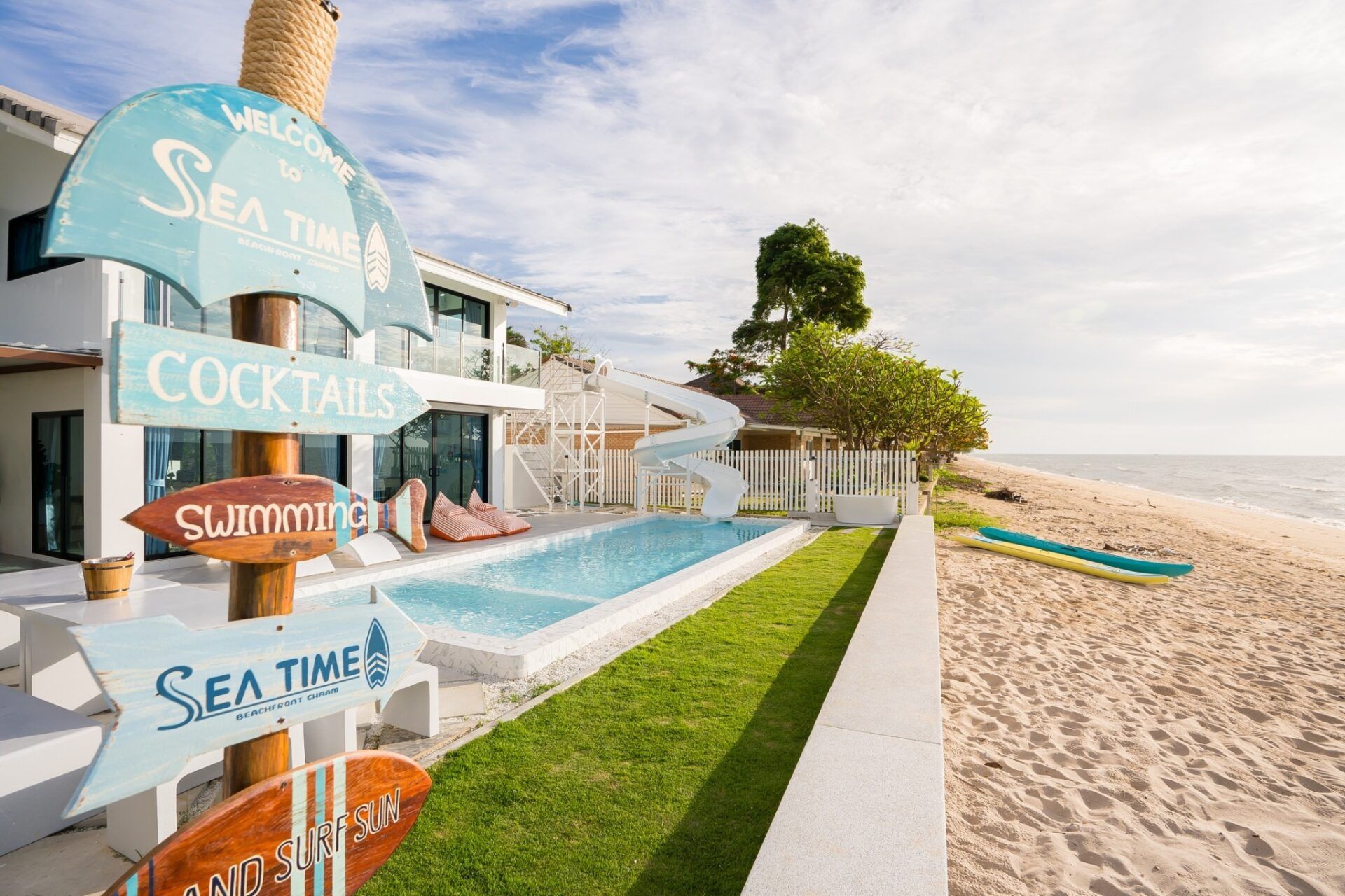 Beachfront pool with slide at Sea Time Villa, Cha-Am. Sign points to cocktails and swimming.
