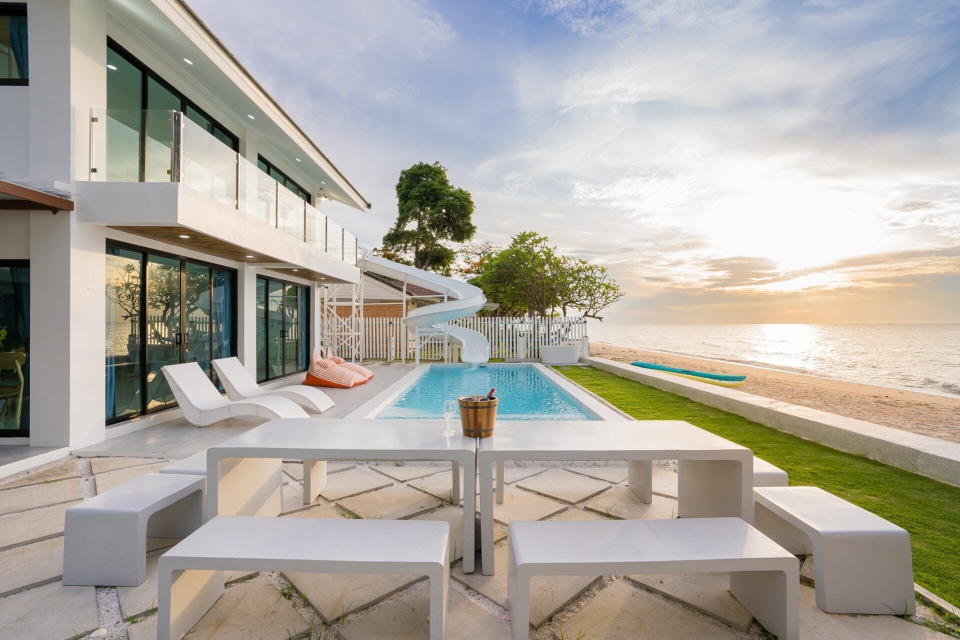 Sunset view of the pool and beach at Sea Time V Pool Villa, Cha-Am. Features a waterslide and outdoor dining area.