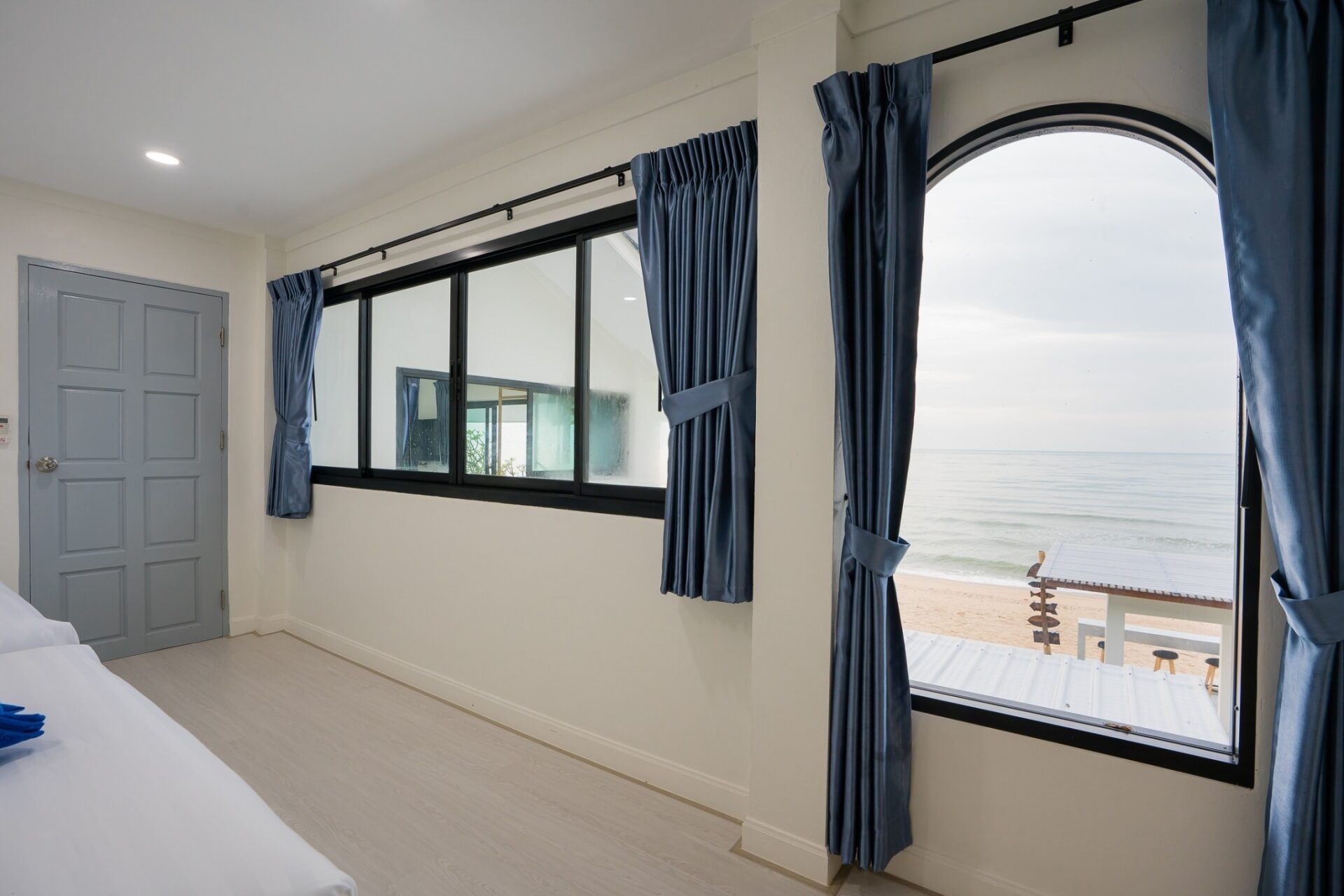 Bedroom view of the ocean at Sea Time V Pool Villa, Cha-Am. Large windows with blue curtains.