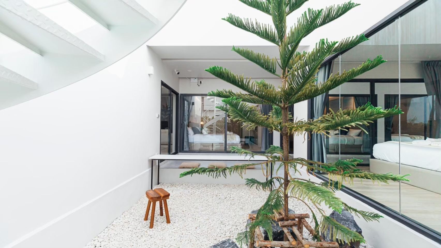 Indoor-outdoor space at Shore Season V Pool Villa, Banglamung. View of bedroom through glass wall, small tree, white gravel.