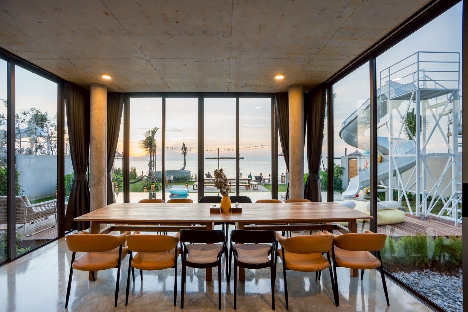 Modern dining table at Spirit V Pool Villa, หาดปึกเตียน-ชะอำ. Ocean view and waterslide visible through the glass walls.