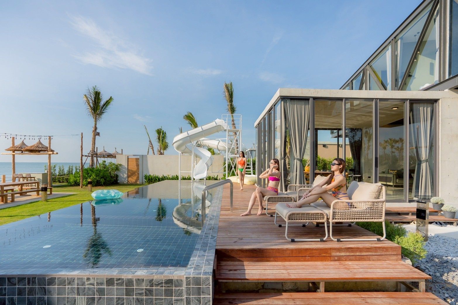 Poolside view at Spirit V Pool Villa, หาดปึกเตียน-ชะอำ. Women relaxing on lounge chairs by the pool and waterslide.