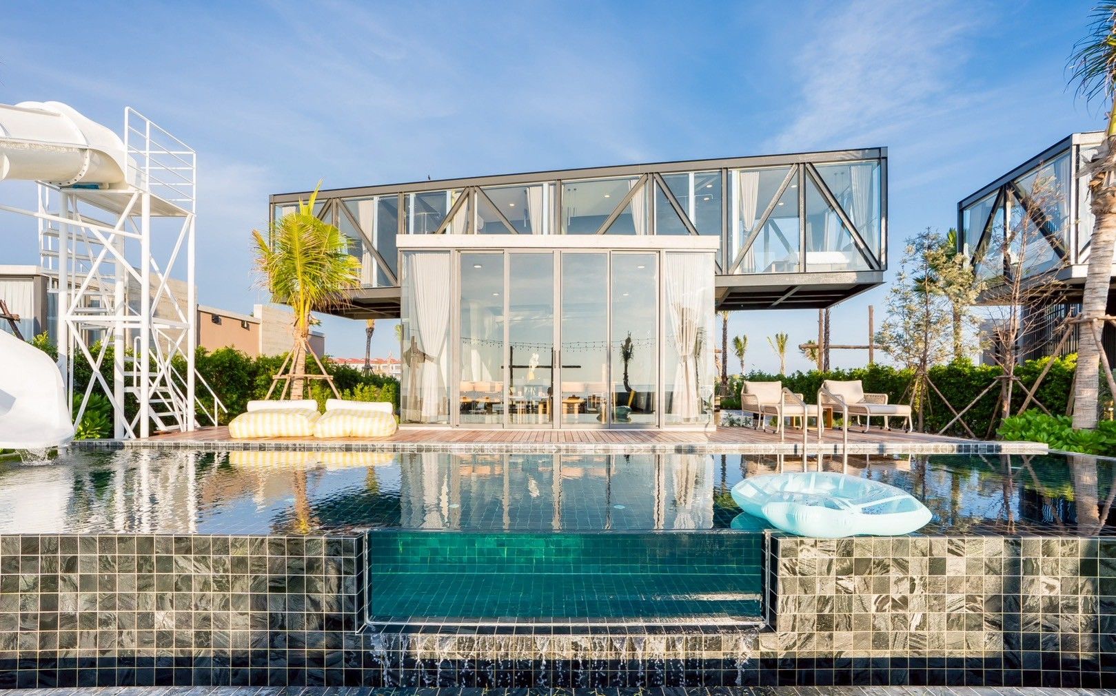 Spirit V pool villa, หาดปึกเตียน-ชะอำ. View of the pool with waterslide and glass-walled building reflecting in the water.