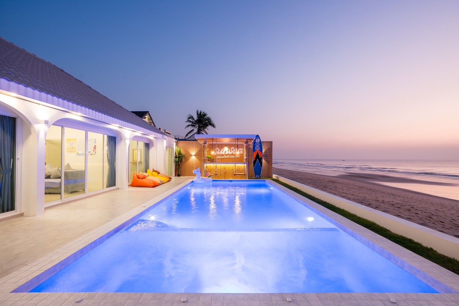 Illuminated pool at Sun Sea V Pool Villa, beachfront in Cha Am. View of the ocean and beanbag chairs on the patio.