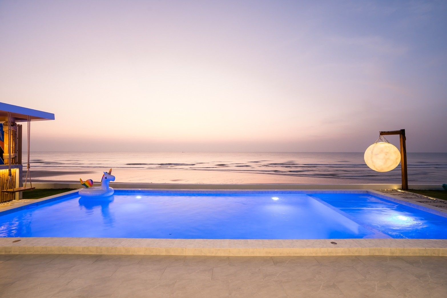 Sunset view from the pool at Sun Sea V Pool Villa, ติดทะเล หาดบางเกตุ ชะอำ. Features a unicorn floatie and illuminated moon l