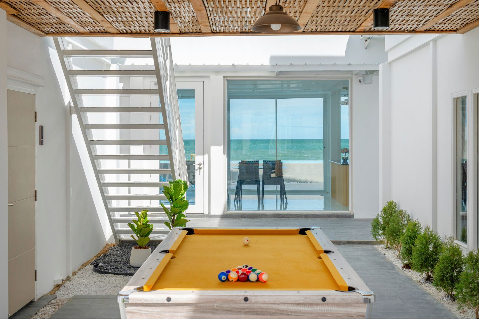 Talay Haus X Pool Villa in หาดเจ้าสำราญ-ชะอำ เพชรบุรี features an indoor pool table with ocean view and white staircase.