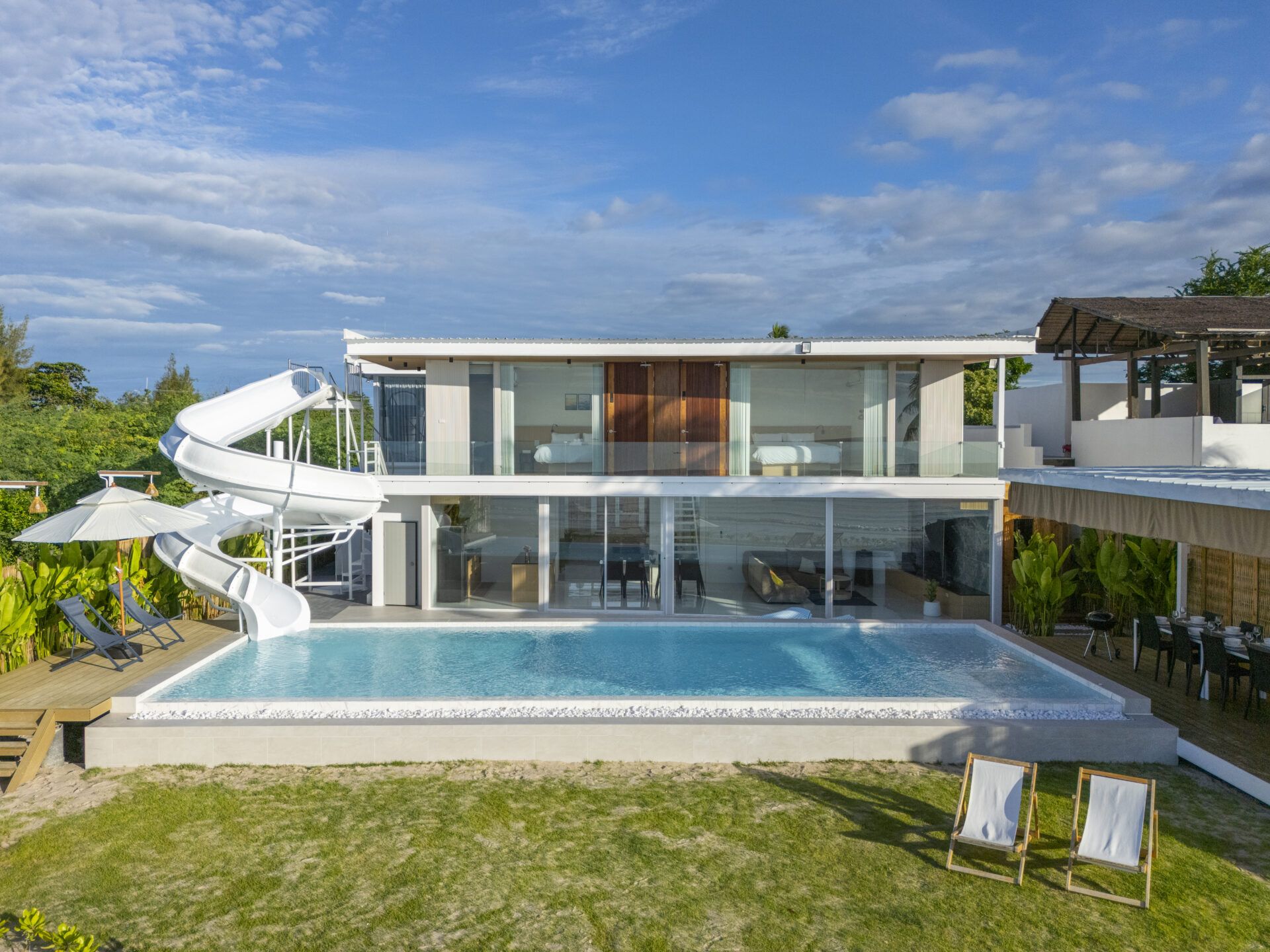 Talay Haus X pool villa in หาดเจ้าสำราญ-ชะอำ เพชรบุรี features a water slide into the pool, deck chairs, and outdoor dining.