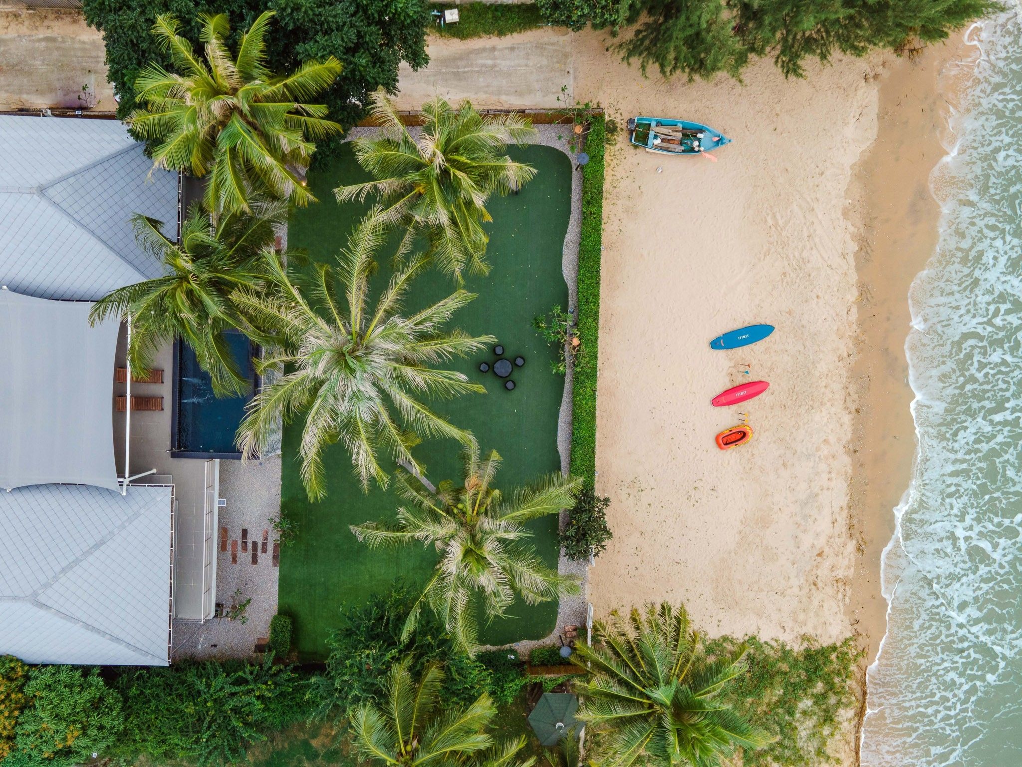 Aerial view of THE PINE V Pool Villa, beachfront property with kayaks and boat on the sand.