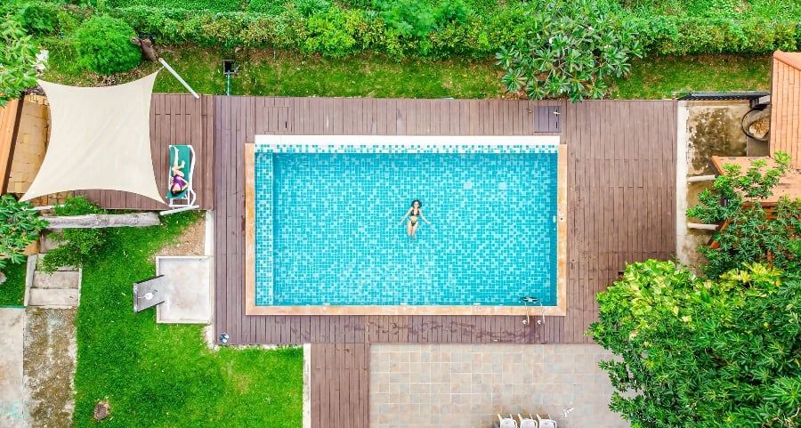 Aerial view of the pool at The Valley Khaoyai IV pool villa. Woman swimming in the blue tiled pool, surrounded by lush greene