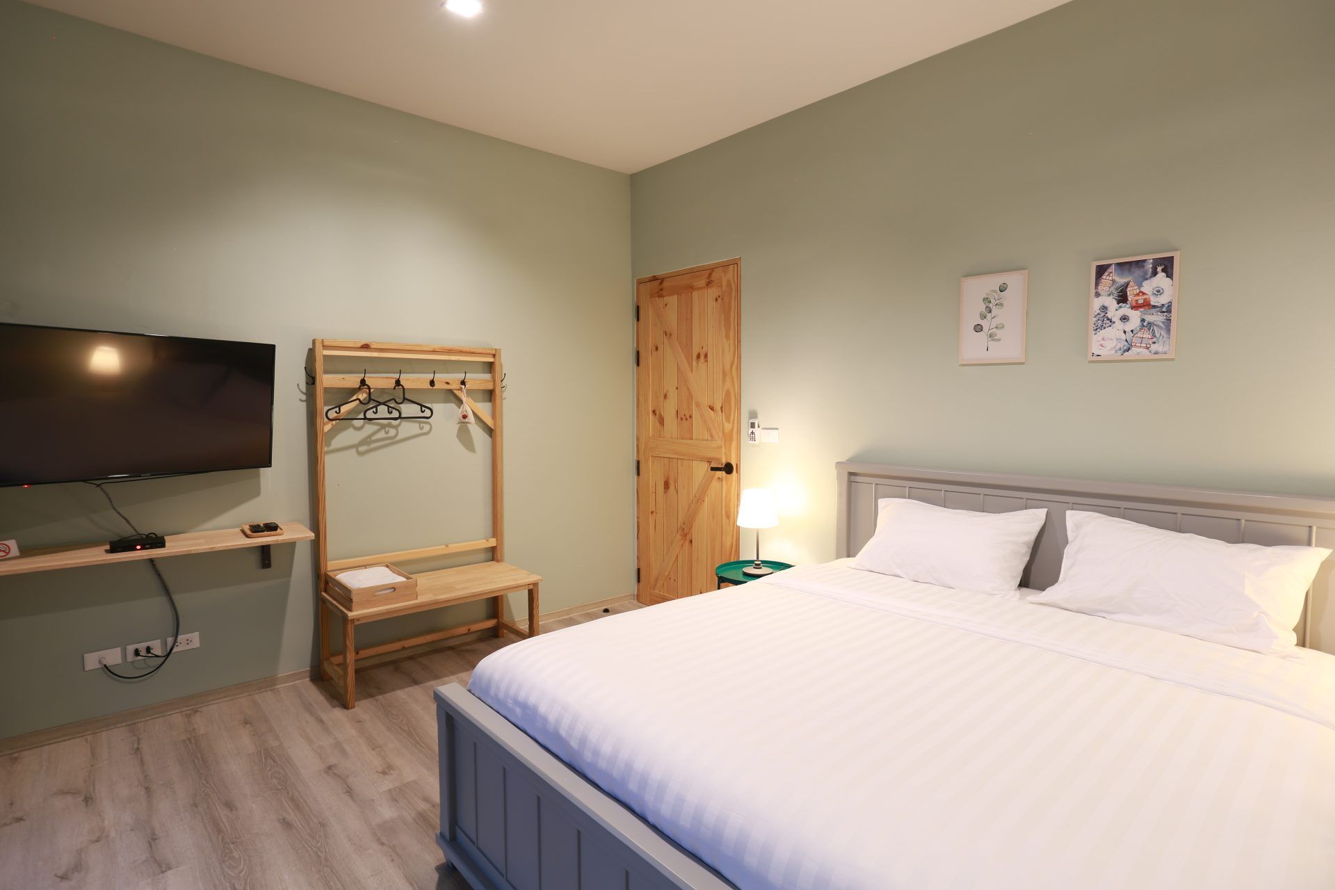 The Valley Khaoyai VI Villa bedroom with white striped bedding, TV, and wooden clothes rack. หมูสี เขาใหญ่.