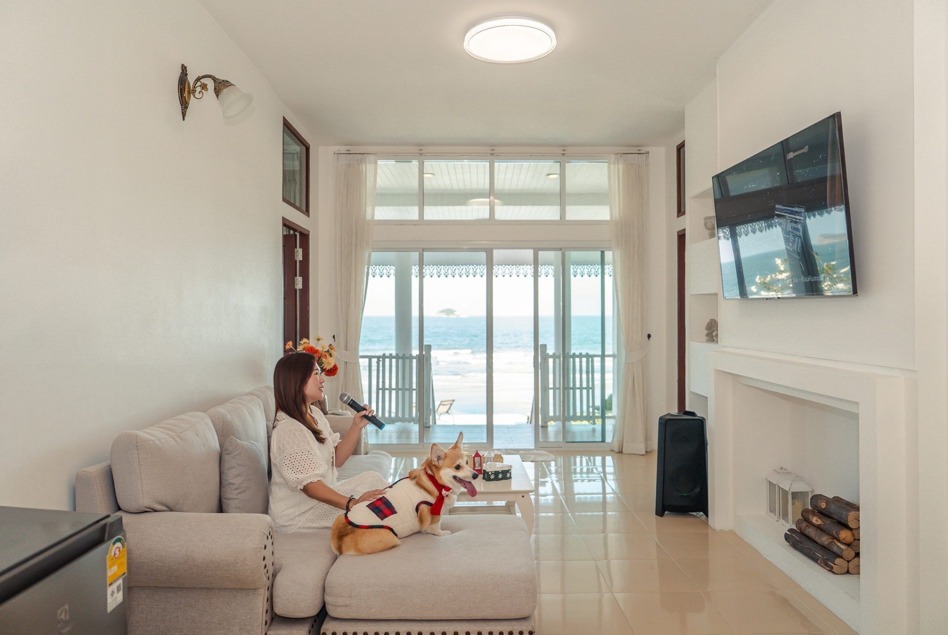 Living room at Twenty-Six Pool Villa Hua-hin. Woman sings karaoke with her dog, ocean view through the windows.