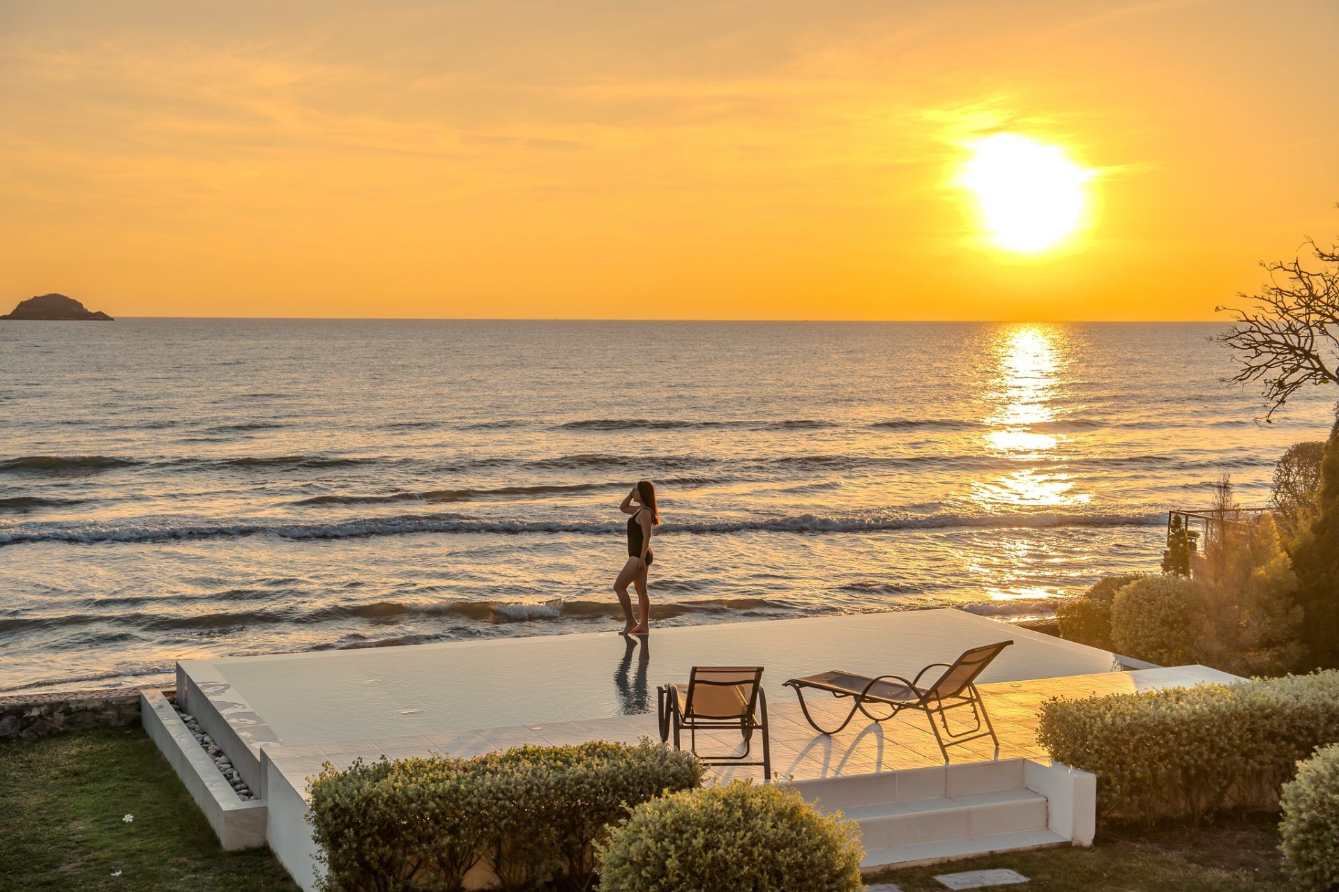 Sunset view from the infinity pool at Twenty-Six Pool Villa Hua-hin, หัวหิน 101 ประจวบฯ. Woman in swimsuit on pool edge.