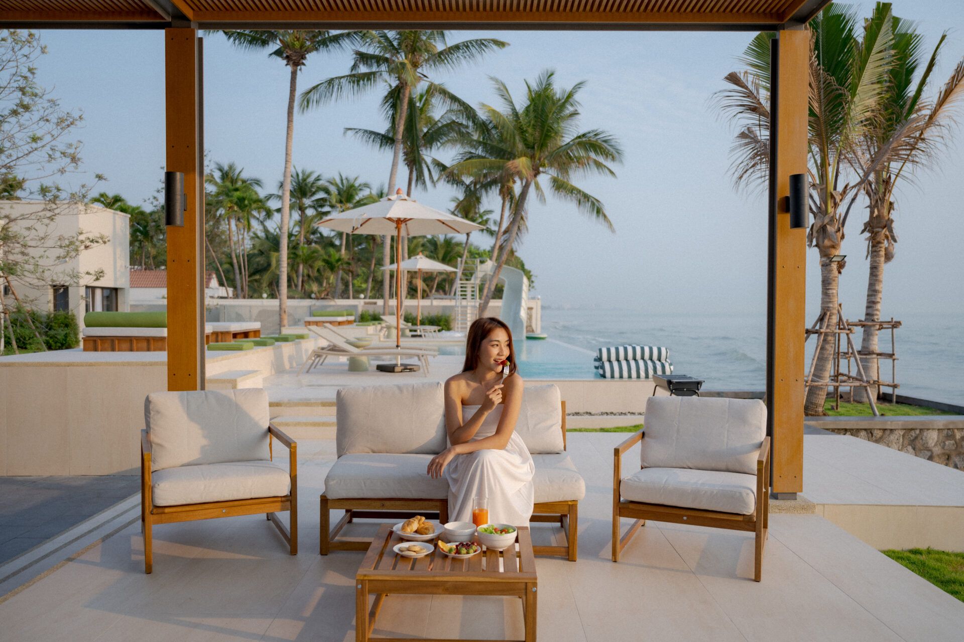 Ocean view from the covered patio at Valika VIII pool villa, Hua-Hin Soi 45. Woman enjoys breakfast on the outdoor furniture.