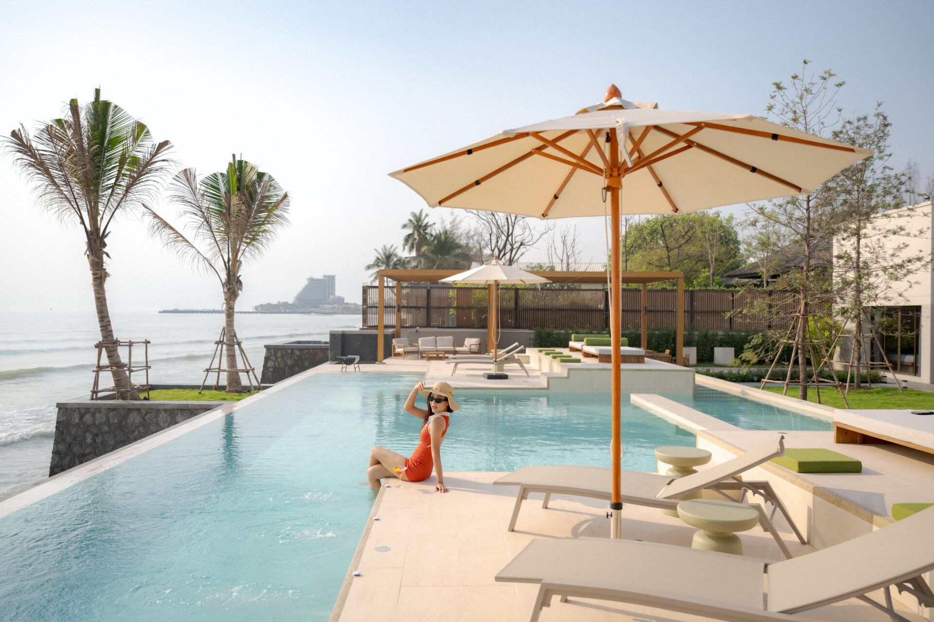 Woman relaxing by the infinity pool at Valika VIII pool villa, Hua Hin. Ocean view with palm trees and lounge chairs.