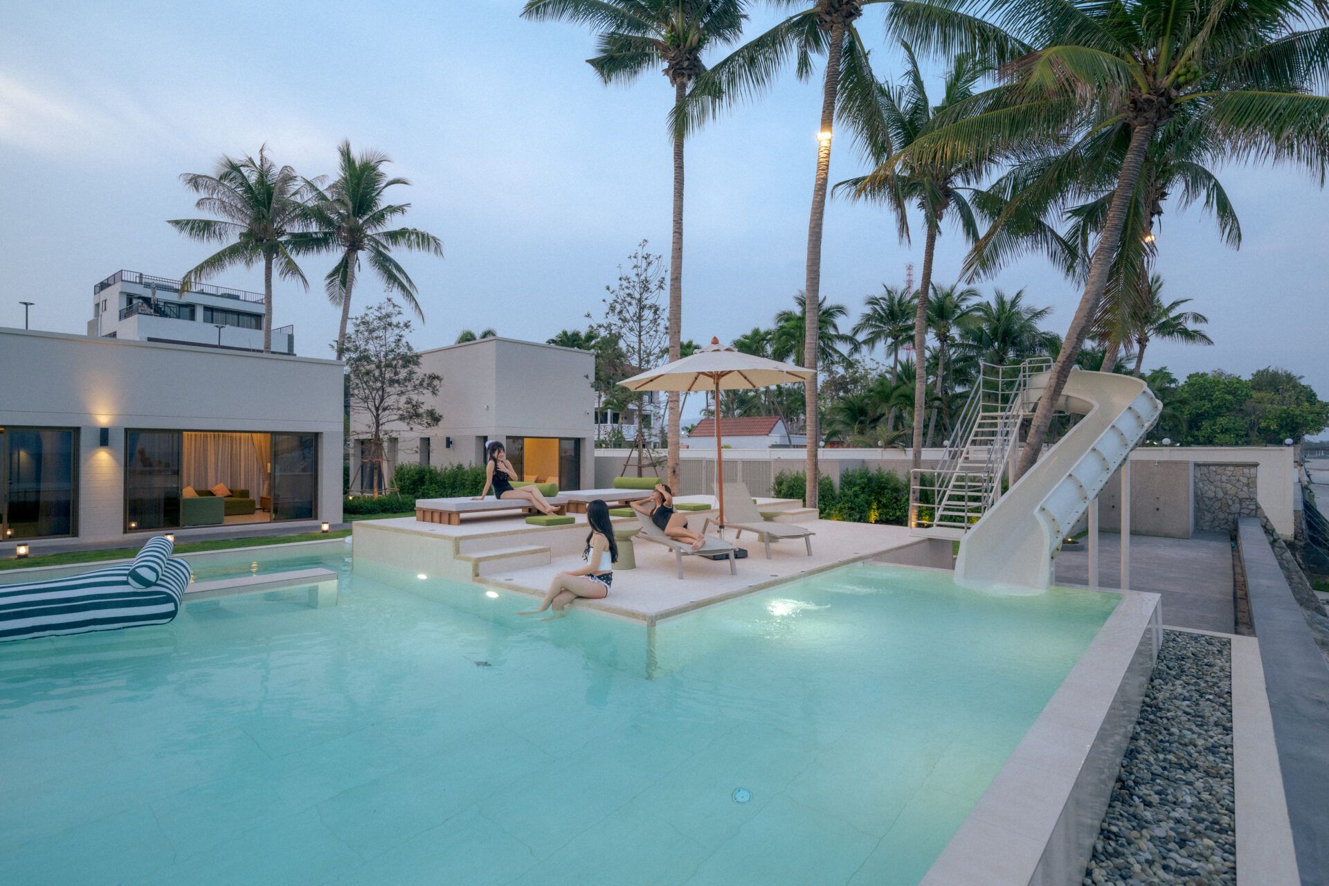 Valika VIII pool villa in Hua Hin, Soi 45. People relaxing by the pool with lounge chairs and a water slide.
