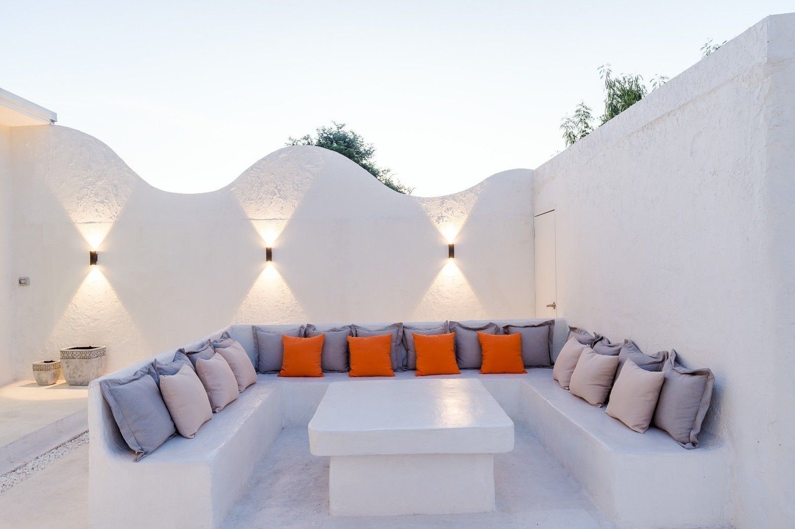 White Coco V Pool Villa sunken outdoor seating area in พัทยากลาง-นาเกลือ. White walls, orange pillows, and modern lighting.