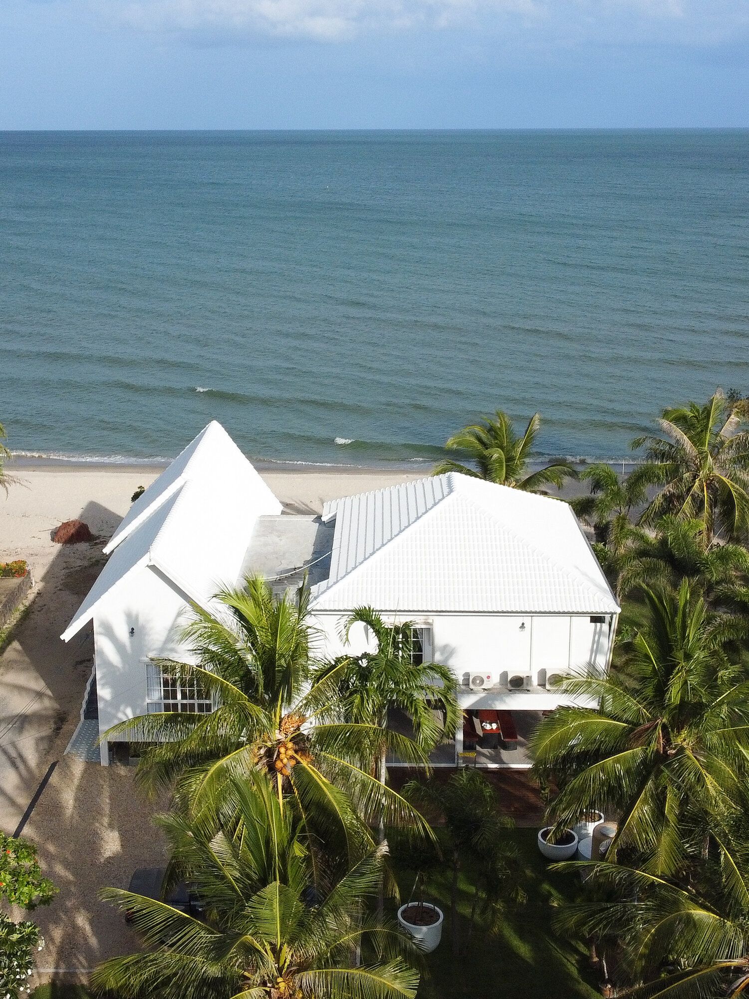 Aerial view of Coastal Calm IV Pool Villa in Cha-Am, showing its white exterior, lush palm trees, and direct beachfront acce