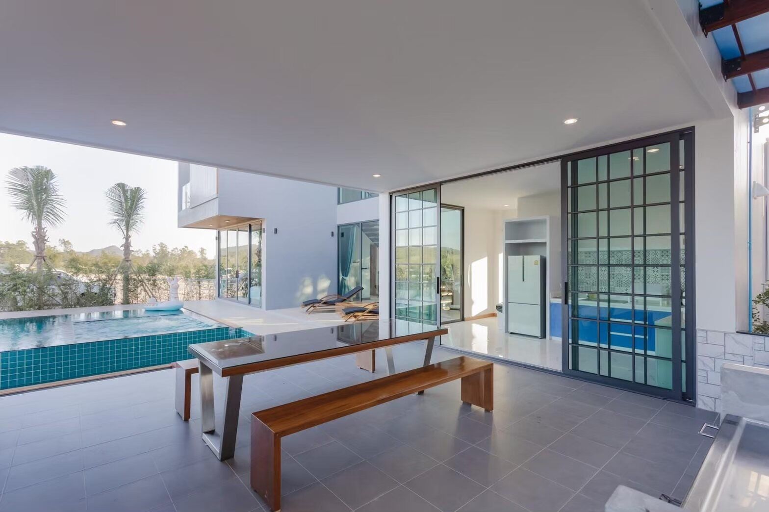 Outdoor dining area with a long wooden bench and glass table, overlooking the pool at Exclusive Proud VII Villa, Hua Hin.