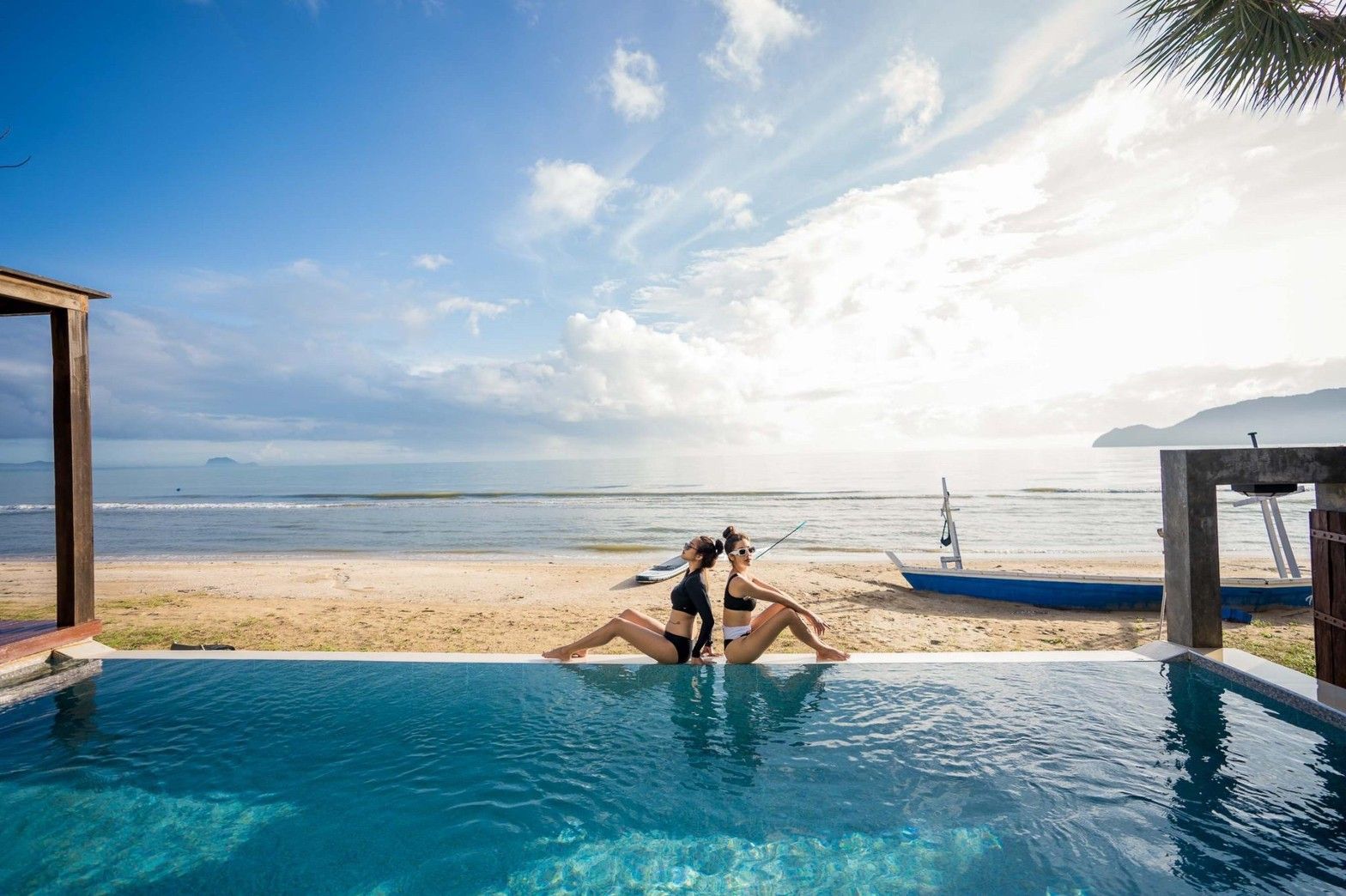 Two women relax by the infinity pool at Marine Pran II Pool Villa, facing the beach in Khao Sam Roi Yot, Pranburi.