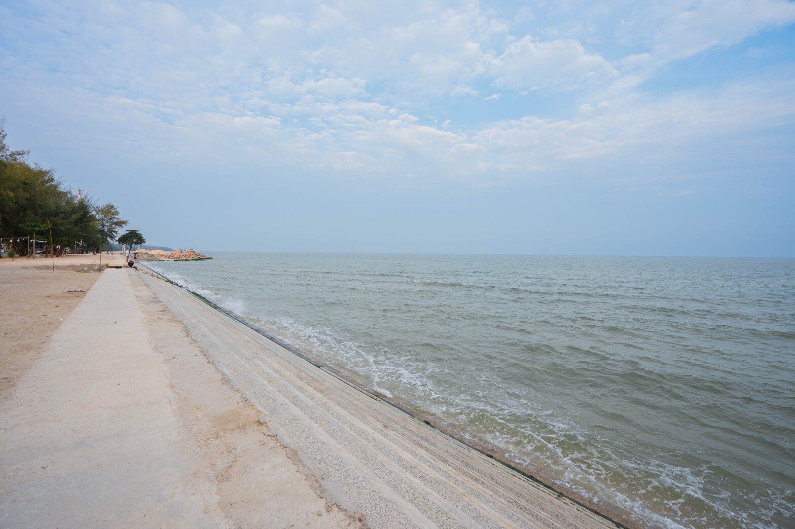 View of the ocean and a concrete seawall path along the beach near Miami Beach VI Pool Villa in Cha-Am.