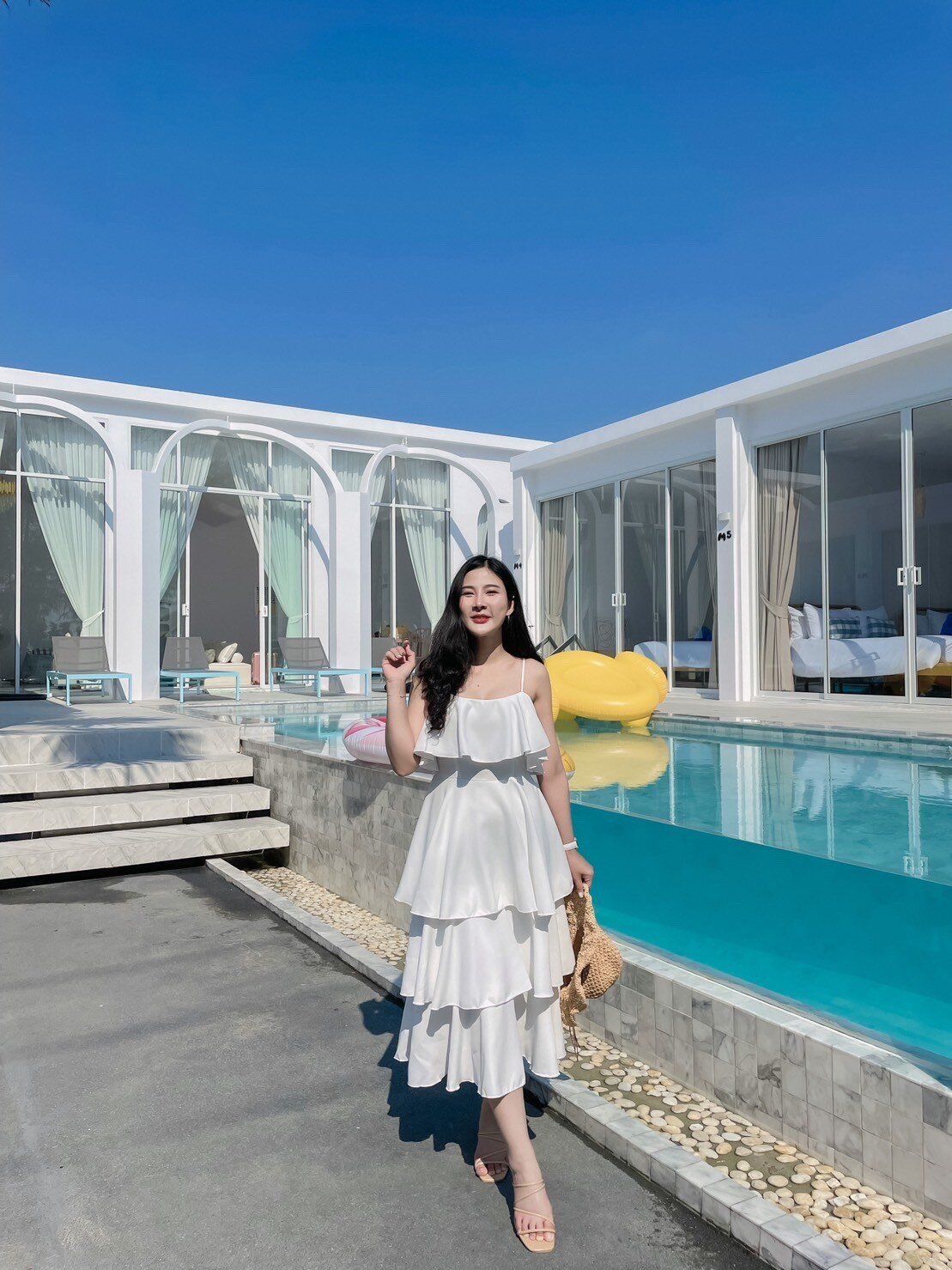 A woman in a white dress stands by the bright blue pool at Miami Beach VI Pool Villa, Cha-Am, on a sunny day.
