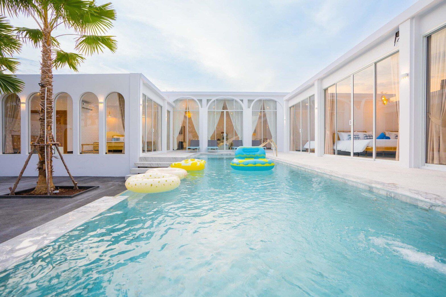 U-shaped swimming pool with yellow and blue inflatables at Miami Beach VI Pool Villa, Cha-Am. Modern white architecture.