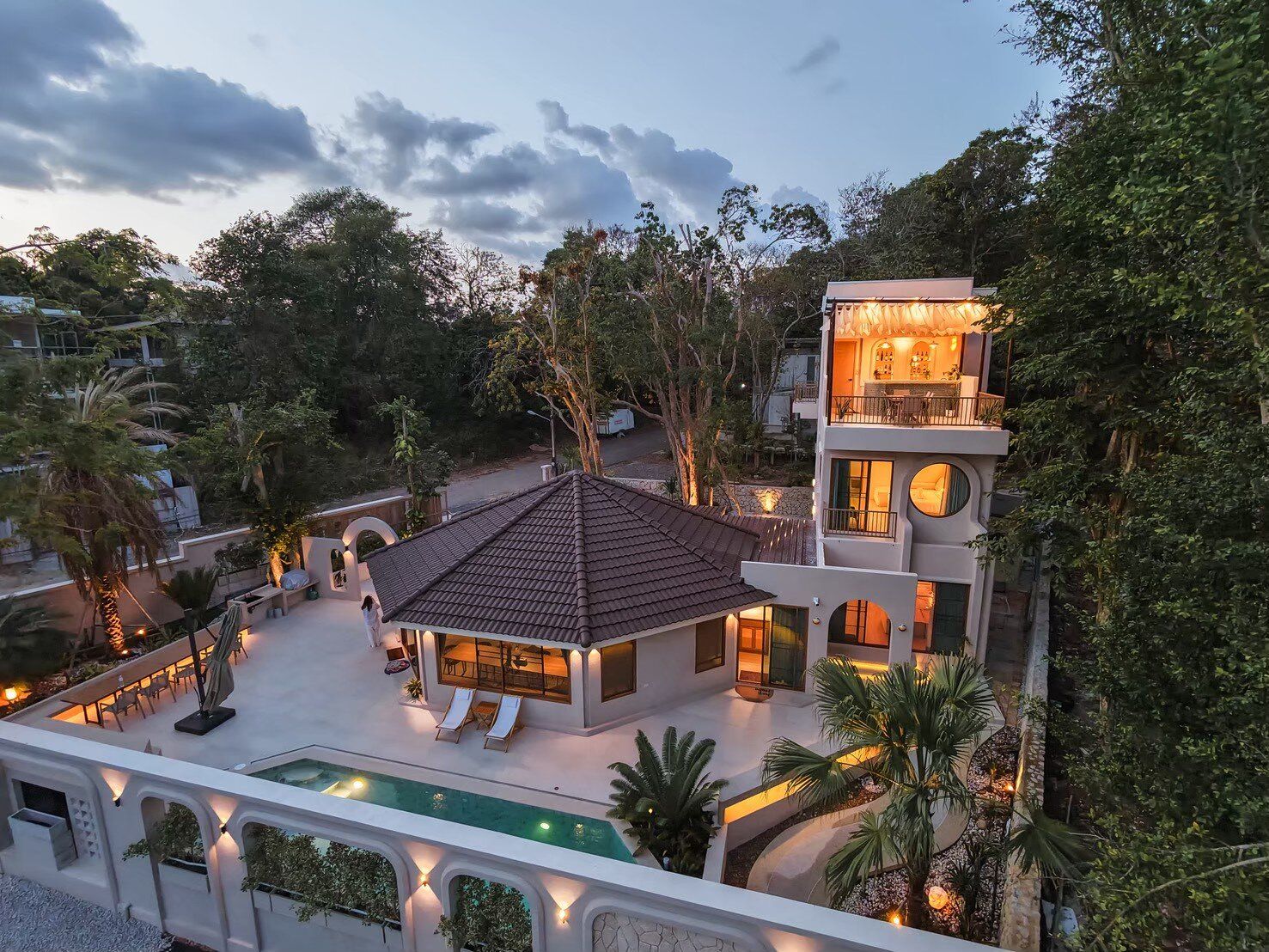 Aerial view of Sand Moment VI Pool Villa in Rayong at dusk, showcasing the illuminated exterior, pool, and surrounding trees.