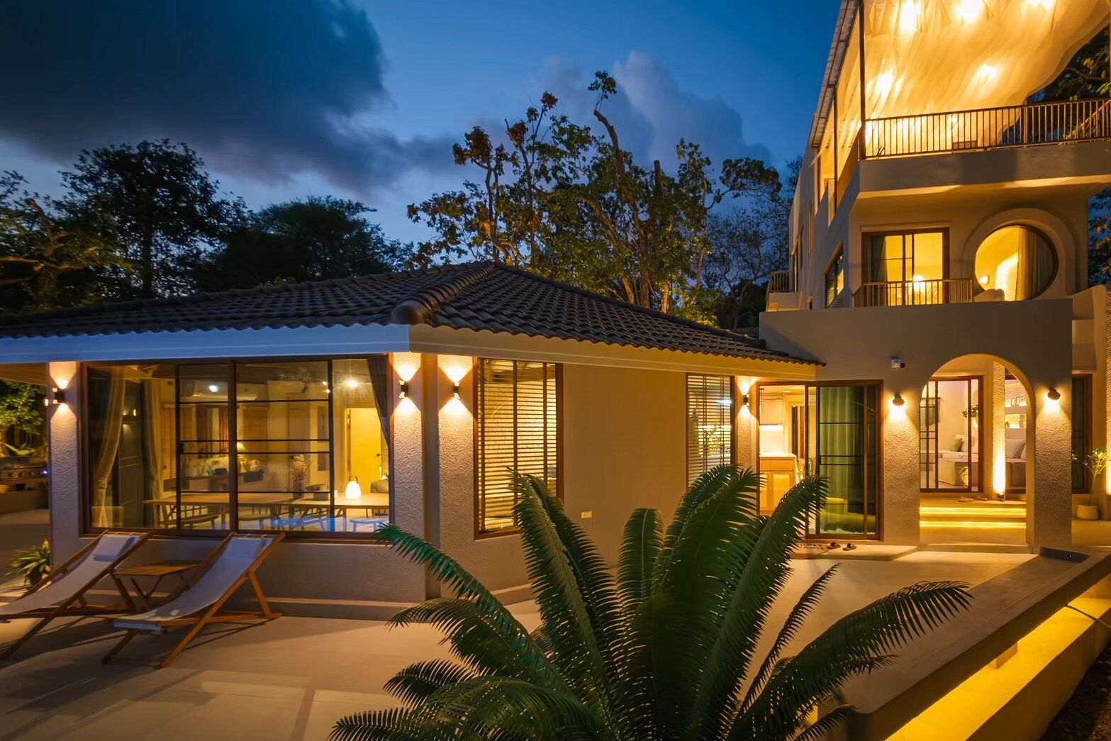 Exterior view of Sand Moment VI Pool Villa in Rayong at dusk, showcasing warm lighting on the facade and lush greenery.