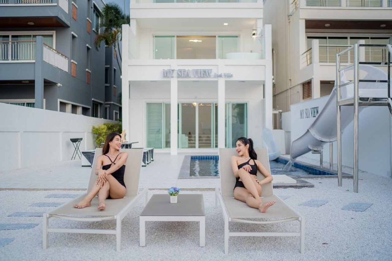 Two women lounge by the pool at Sea View IV Pool Villa in Pattaya. Waterslide visible. Relaxing poolside at this Thailand vil