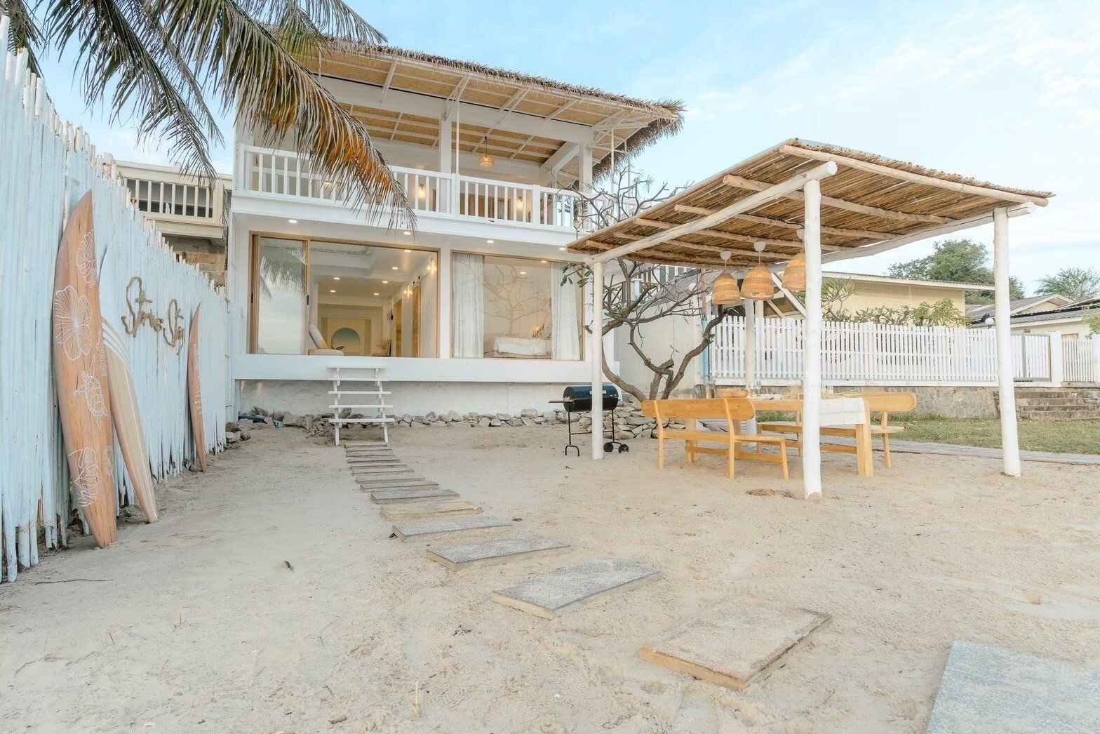 Story II Pool Villa Hua-Hin's beachfront exterior with a thatched roof, outdoor dining area, and BBQ grill on the sand.