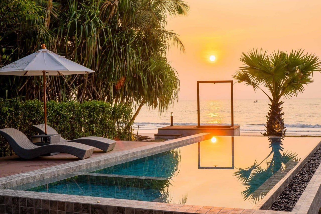 Stunning sunset over the beachfront pool at Studio Beachfront III Pool Villa in Cha-Am, Thailand, with lounge chairs and ocean views.