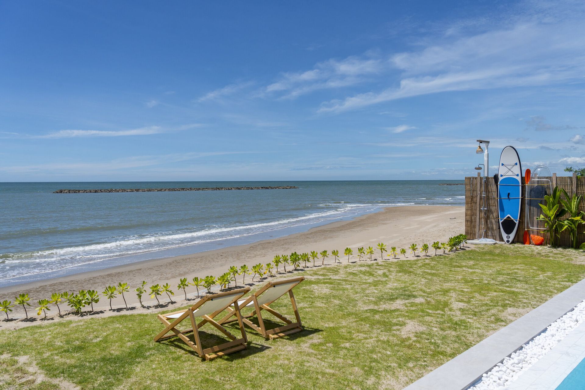 Beachfront lawn at Talay Haus X Pool Villa, Cha-Am, with two lounge chairs, paddleboard, and kayak by the sea.